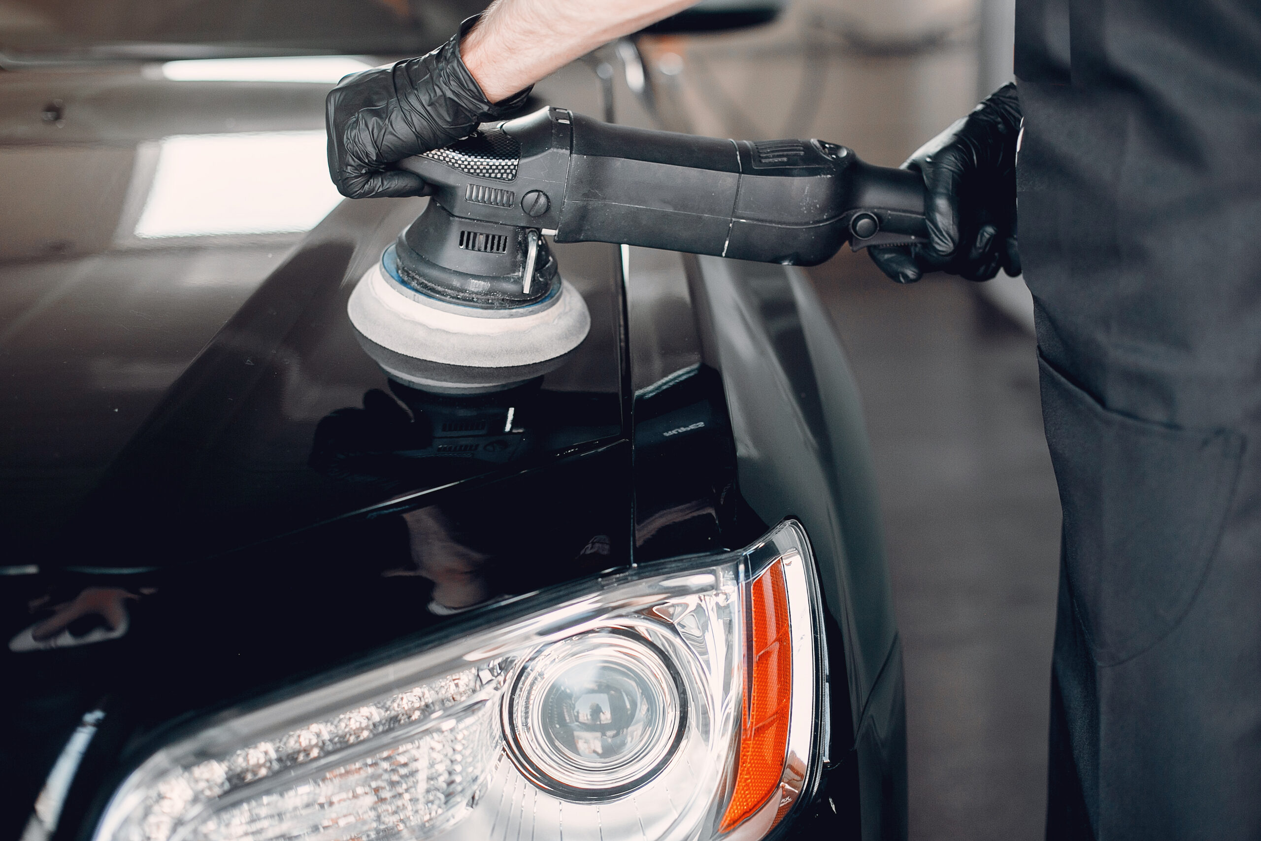 Man in a garage. Worker polish a car.